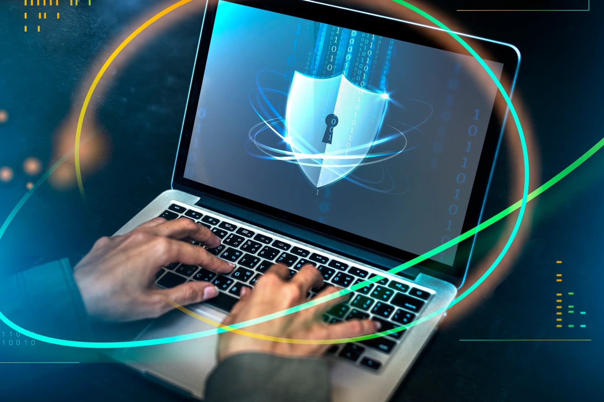 A hooded figure typing on a laptop in a darkened room